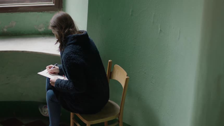 A girl writes in a book by a window