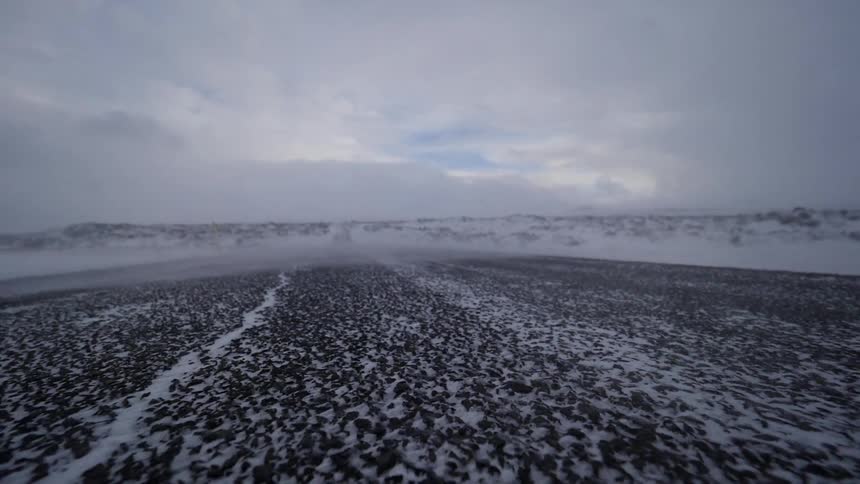 Snow is drifting across the ground as the wind blows