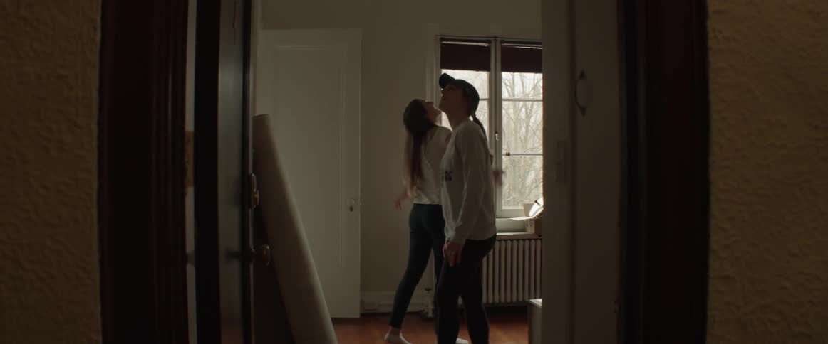 Two women walk through a doorway and look around new apartment