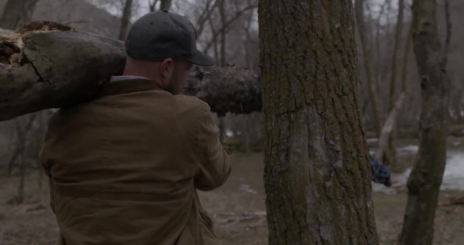 Two people carry a large log through the forest
