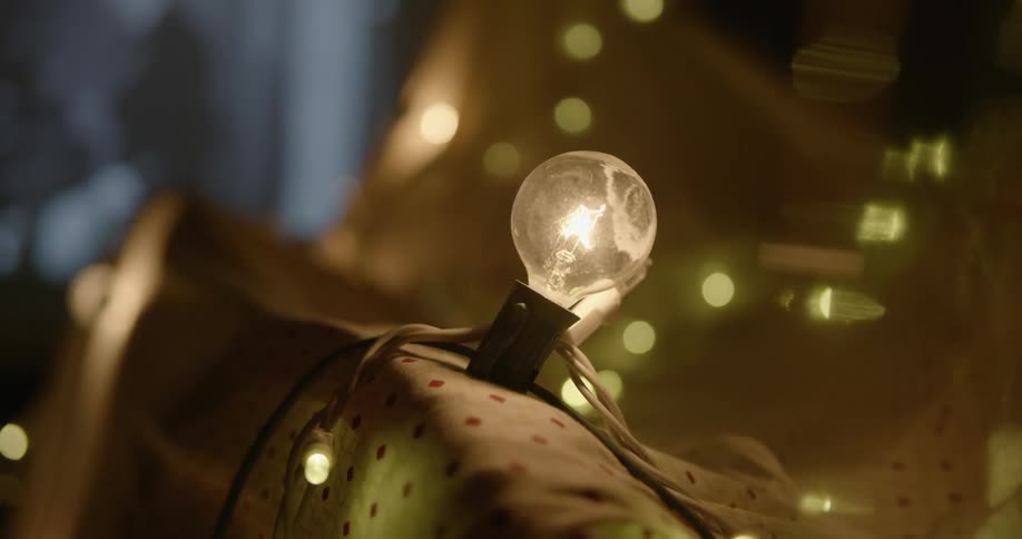 A light bulb and string lights are shining while a tv plays in the background