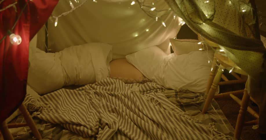 A tent with blankets and pillows on the floor and lights hanging overhead