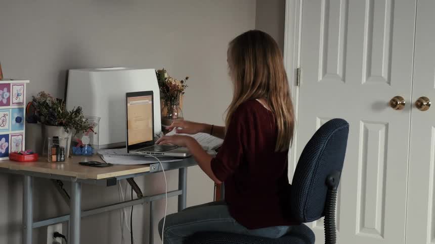 A girl sits at a desk and types on her laptop