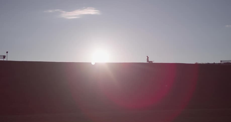 A person is walking a dog on a ridge top during the day