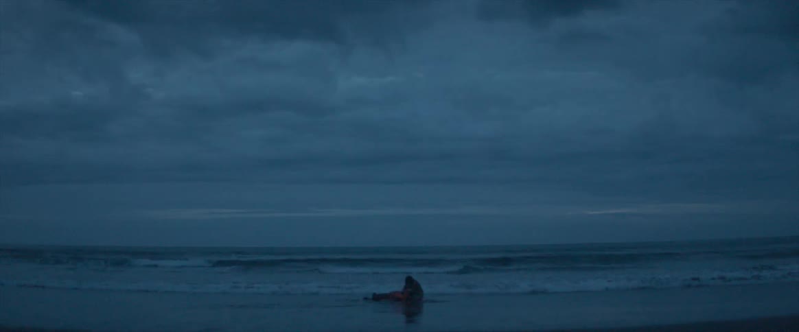 A person is lying near the coast by the water