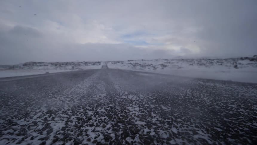 The wind blows snow over the road