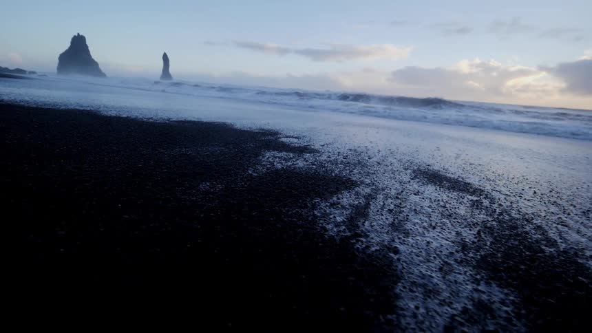Mist hangs in the air above a beach as waves roll ashore