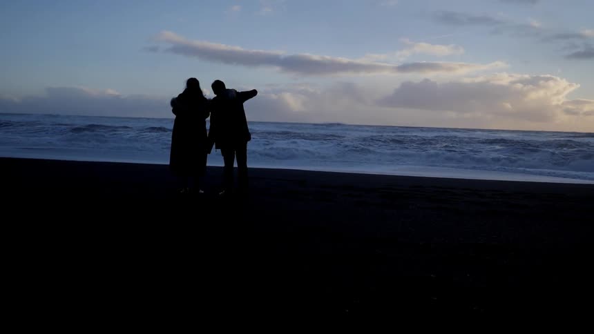 Two people watch the ocean at dawn
