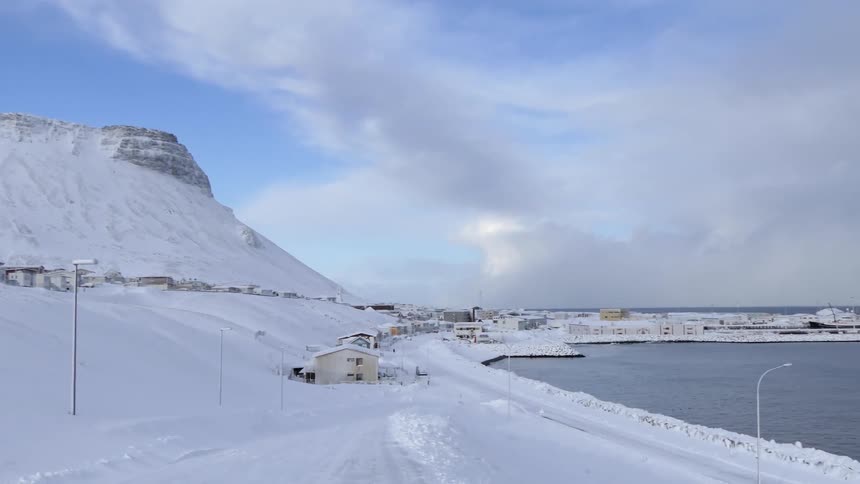 The snow covers a hill and several buildings near a lake