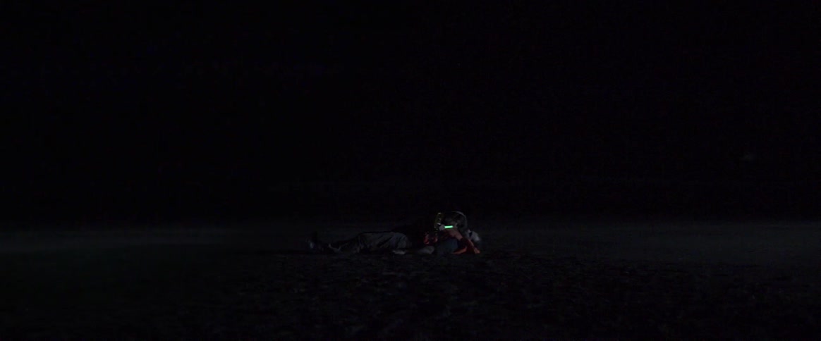 Two people lying together holding a glow stick in the dark