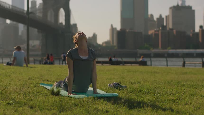 Woman practicing yoga in the park next to a bridge and buildings
