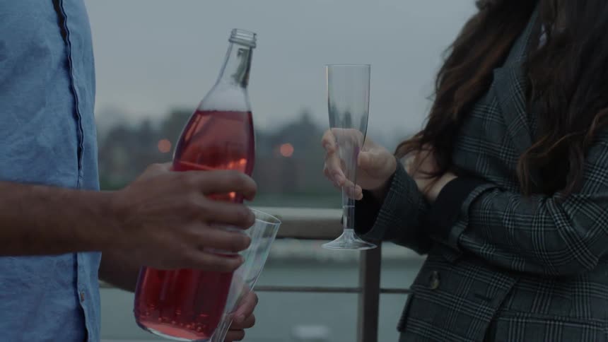 A man and woman drink champagne on a city balcony