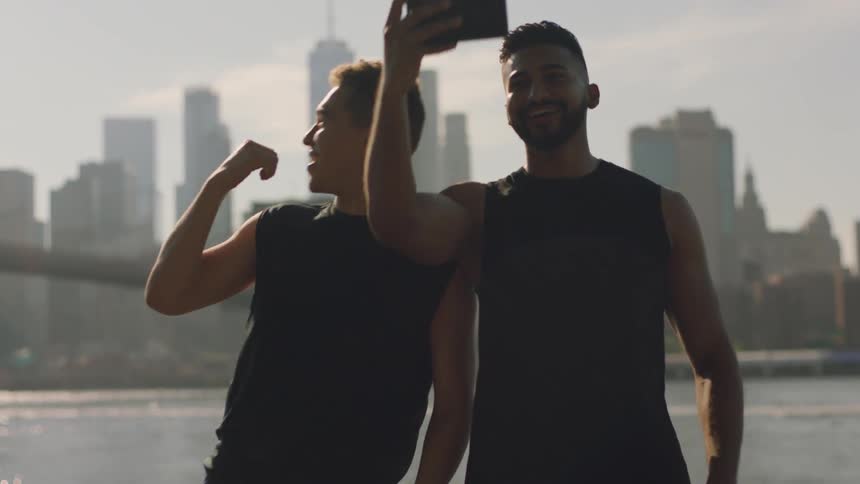Two men take a photo together by the water and city skyline