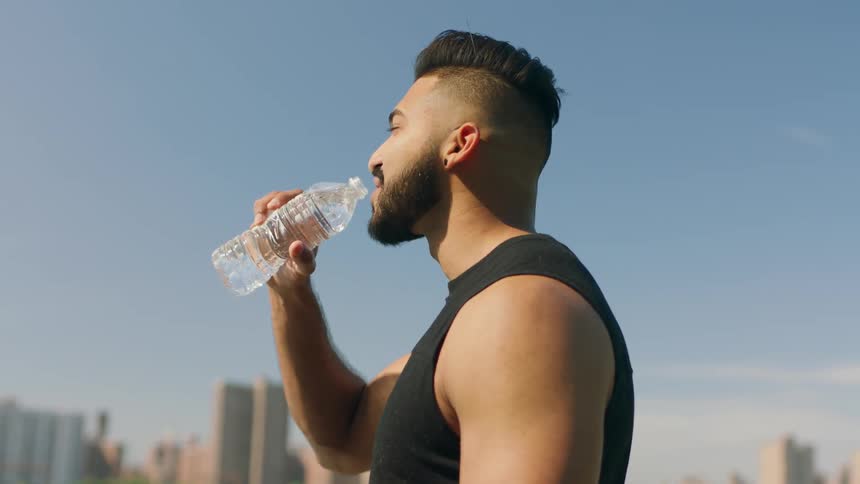 A man sips from a water bottle by the water