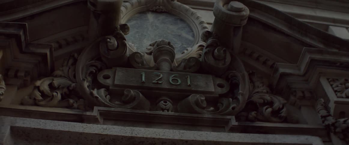 Ornate cement building with numerals sit under a cloudy sky