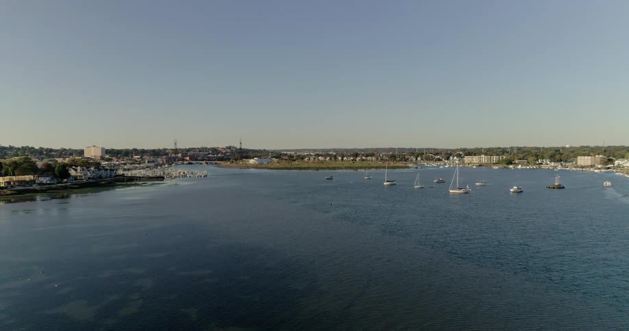 Boats sit anchored in the harbor of a coastal town on a sunny day