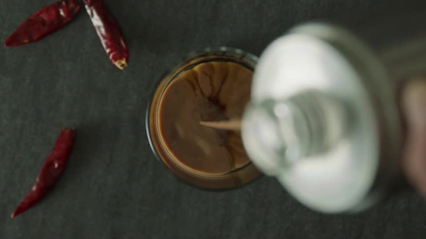 Cream being poured into a cup of coffee with chili peppers on a table