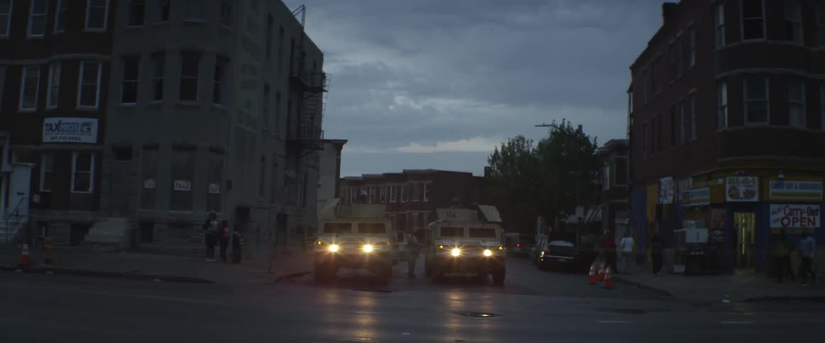 Two humvees are parked in the middle of a side street on a busy city street