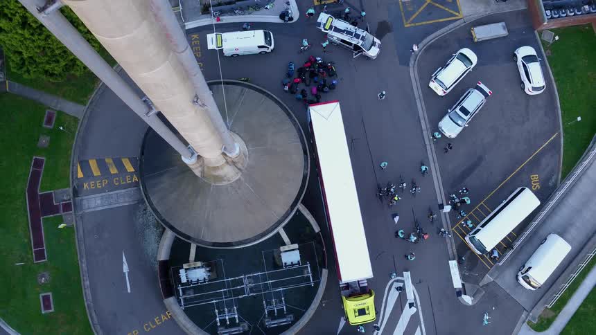 People walk on the asphalt below a large concrete silo