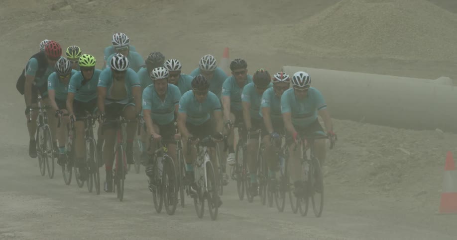 Dust blows over a group of cyclists as they ride