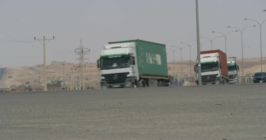 A line of trucks and vehicles travel along a highway during the day