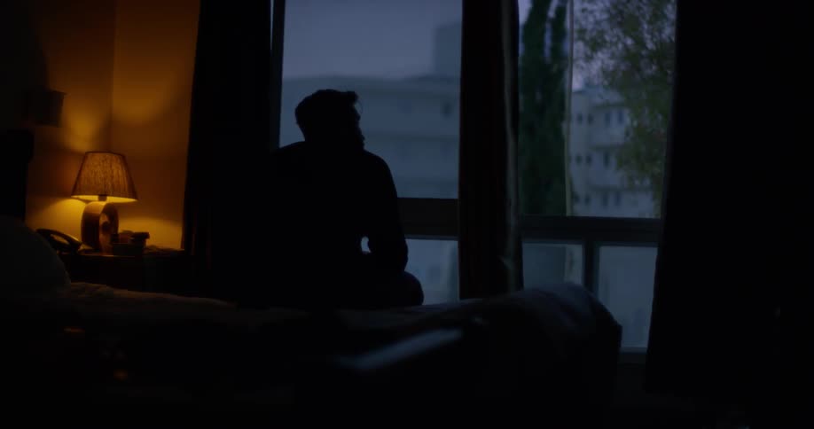 A man sits solemnly on a bed