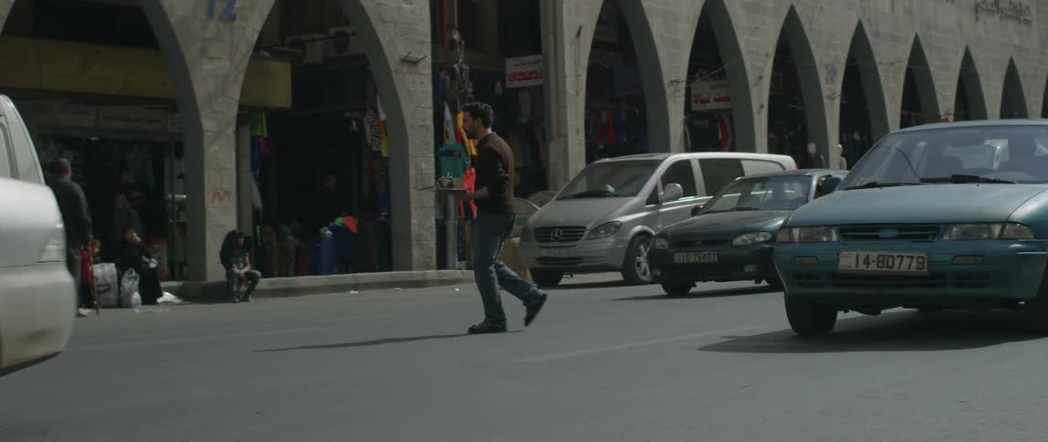 A man crosses a busy street in an middle east city during the day