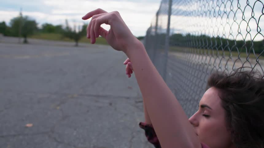 A woman sitting against a chain link fence is lowering her arms