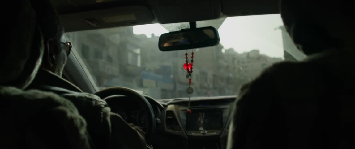 People ride in a car with a rosary hanging from the rear view mirror