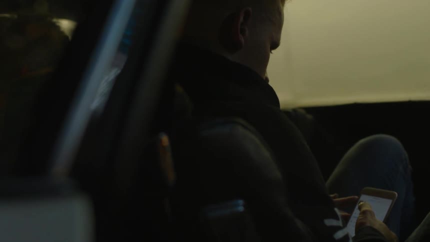 A man sits in a car looking at his phone
