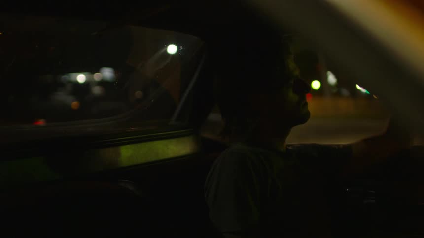 A man sits in a parked car at night
