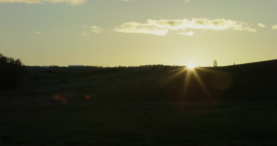 The sun begins to rise over a hill and open field