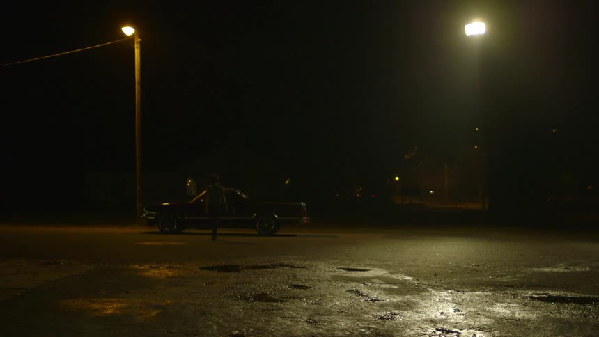 A young man walks to and enters a car at night