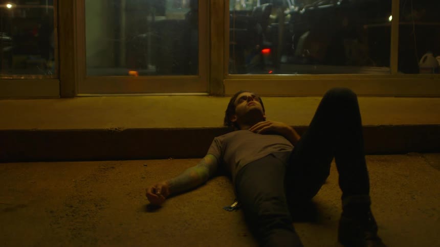 A man is lying in the gutter at night by a building