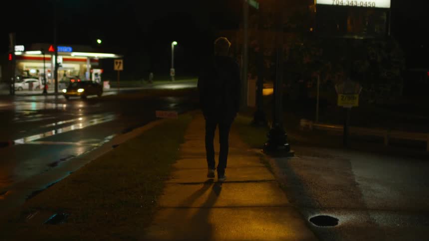A man walks down a wet sidewalk