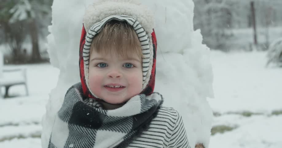 Young child smiles as she stands near a snowman
