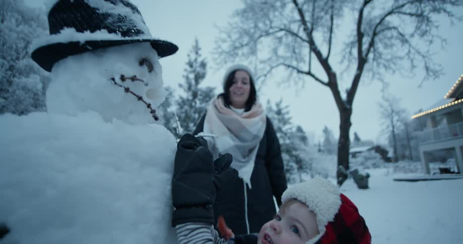 A young boy tries to put a carrot on a snowman