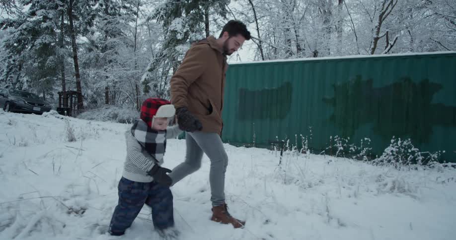 A guy and a child hold hands as they walk through the snow