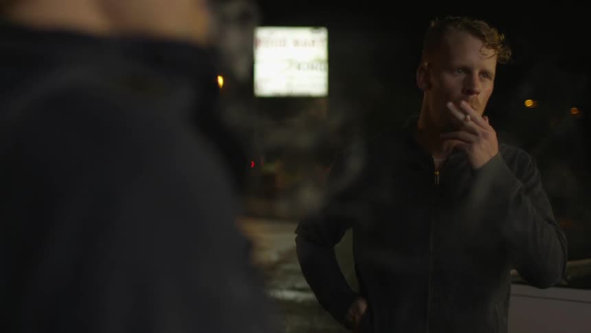 Two men smoke cigarettes outside at night