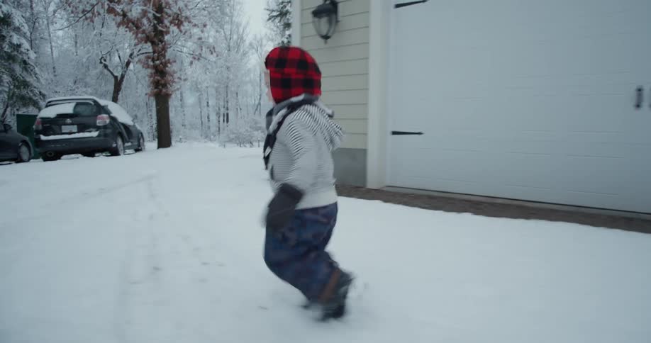 A young boy runs through snow in a snowsuit