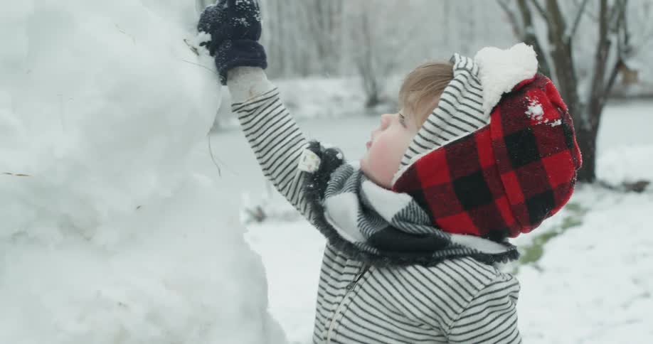 A young child is putting the final touches on a snowman
