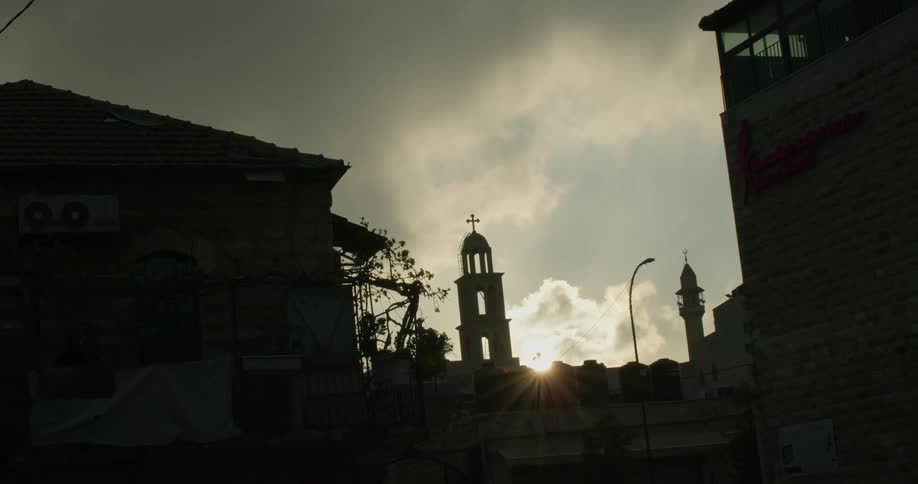 The sun shines beyond a church's bell tower on a cloudy day