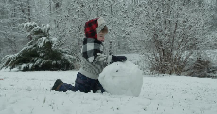 A boy is rolling snow building a snowman
