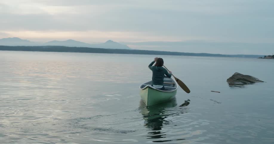 A woman paddles a boat on a mountain lake