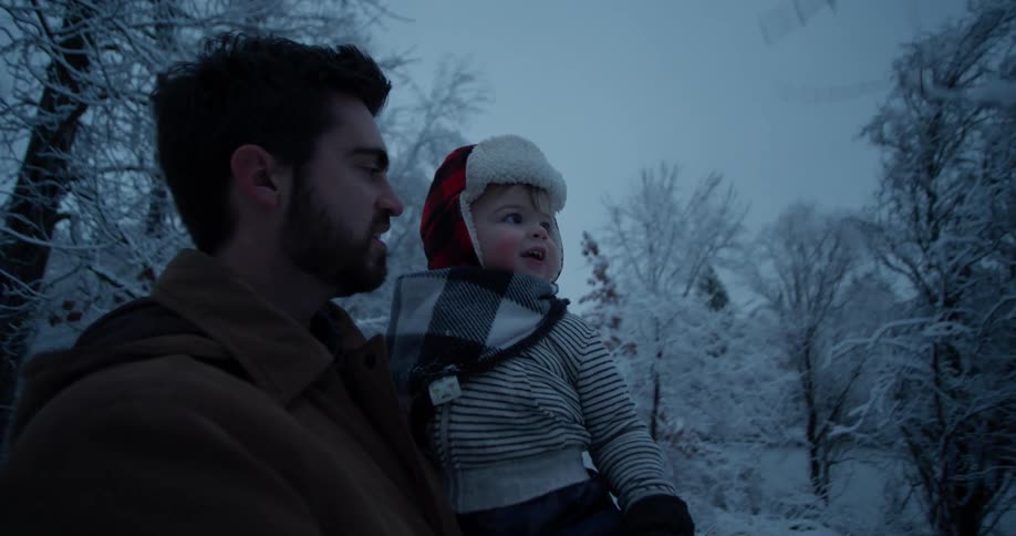 A man shakes a snowy tree for a child
