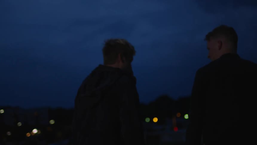 Two men walk outside in the dark