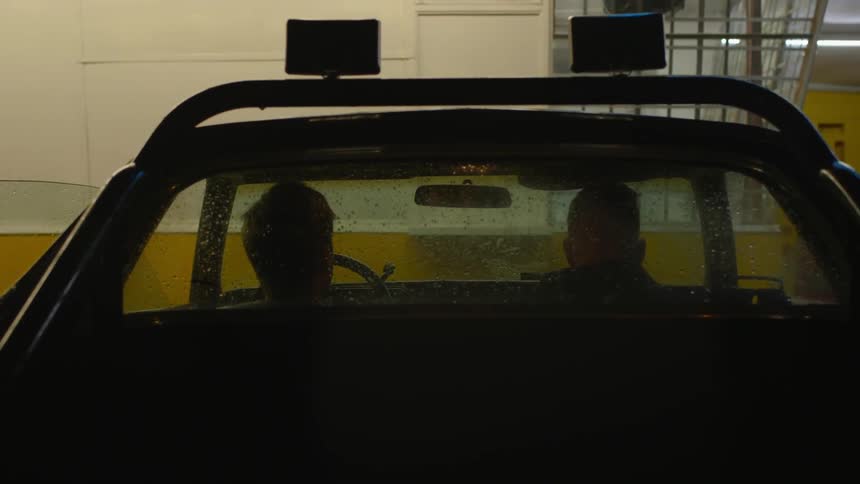 Two men sit in a parked car