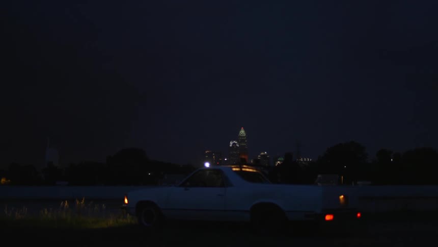 A car is parked on the outskirts of a city watching a lightning storm