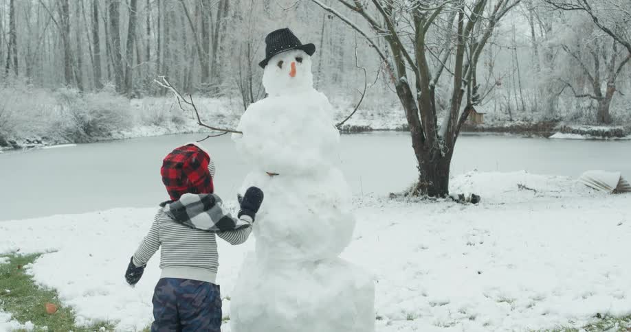 Child pats snow onto a snowman