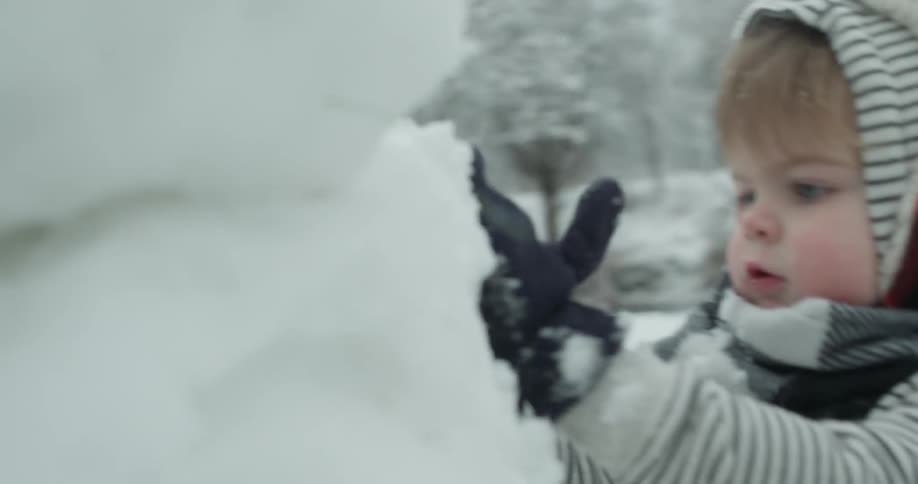 Young child picks up a pile of snow and puts it on a snowman